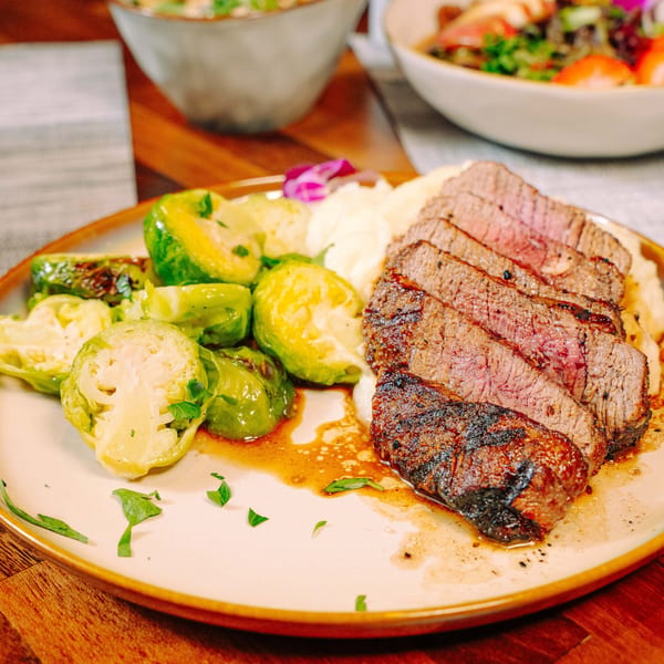 Sliced steak with mashed potatoes and roasted Brussels sprouts on a plate.