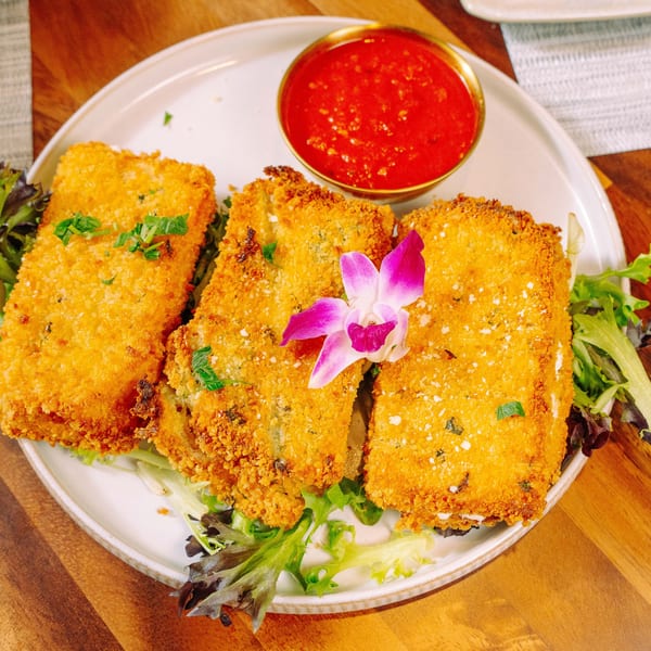 Three golden-brown fried ravioli on a bed of greens with a side of red marinara sauce.