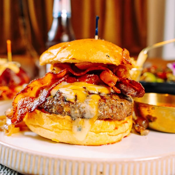 Close-up of a juicy bacon cheeseburger with melted cheese and caramelized onions on a white plate.