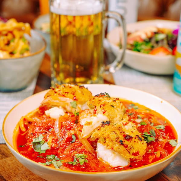 Seafood pasta with red sauce and basil, with a beer mug and salad in the background.
