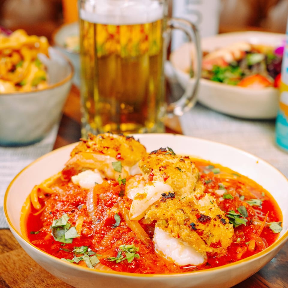 Seafood pasta with red sauce and basil, with a beer mug and salad in the background.